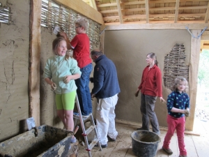 Es macht offensichtlich Spa&szlig;, mal so richtig mit dem Lehm zu matschen. Im Hintergrund ist die erste fertige Innenwand zu sehen.